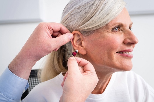 Seniorin bekommt Hörgerät angepasst, Hörakustiker unterstützt bei moderner Hörhilfe.